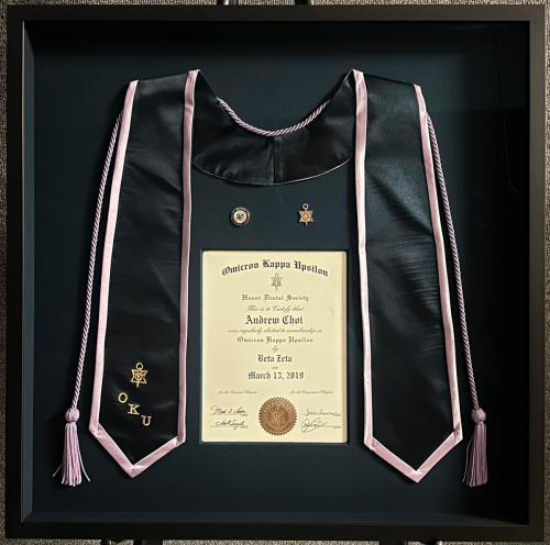Graduation mementos display with certificate, sash, and gold pins in a shadow box.