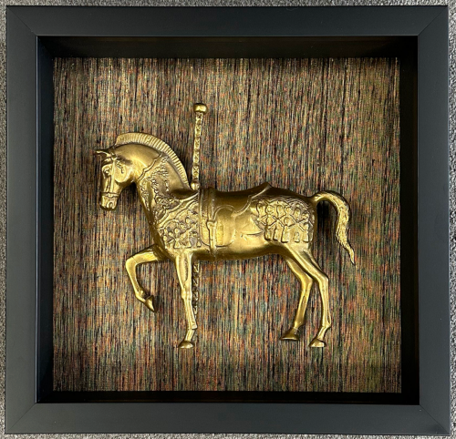 Golden horse ornament mounted in a dark shadow box.